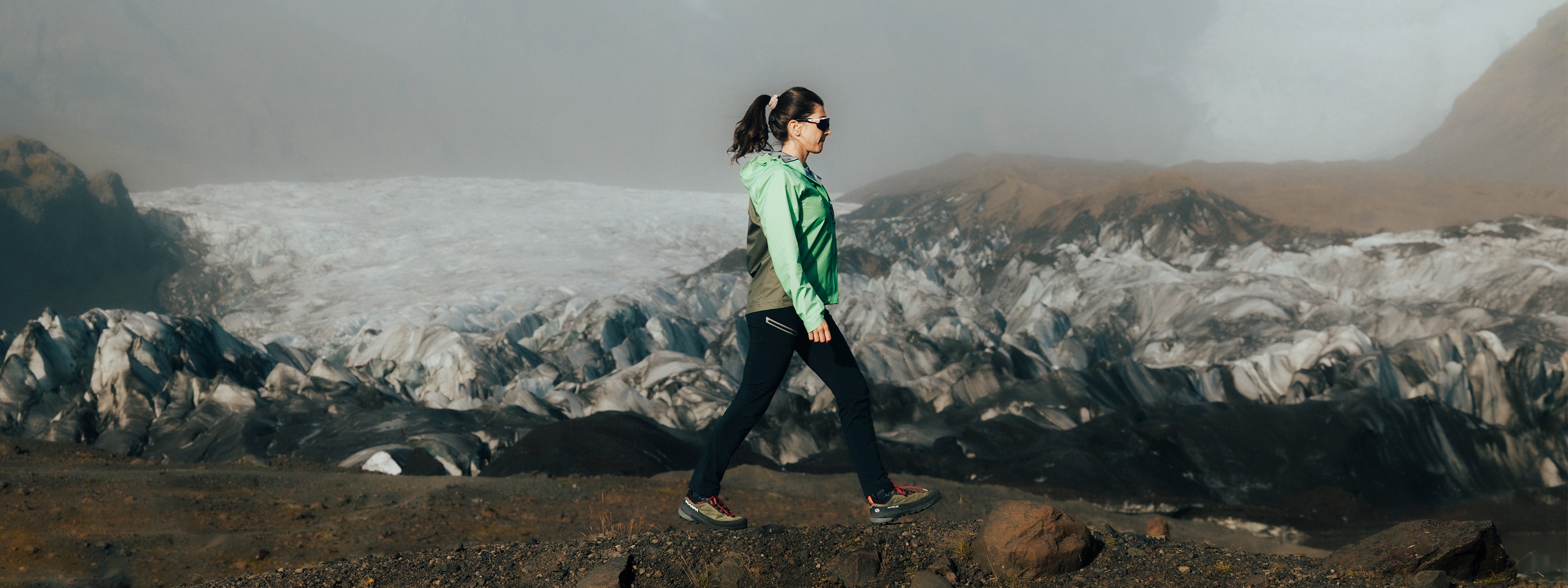 Girl walking on a rocky path with a glacier in the background wearing SCARPA's Rapid XT approach shoes