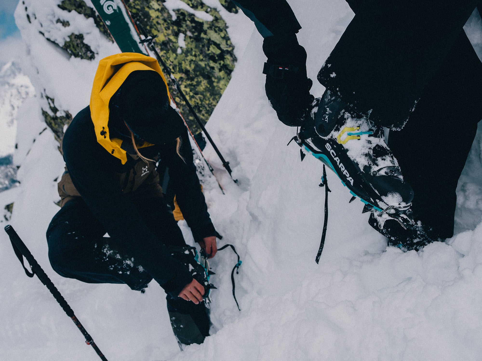 Two skiers in deep snow while adjusting crampons on SCARPA's F1 XT ski mountaineering boots.