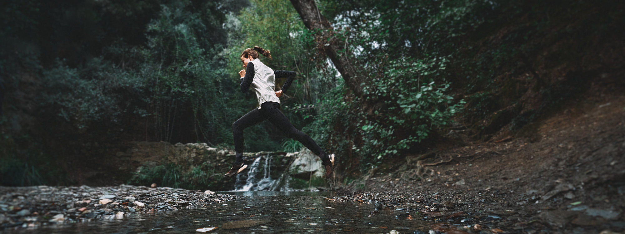Trail runner jumping over a small stream in a forested outdoor setting wearing SCARPA's Golden Gate LT WP trail running shoes.