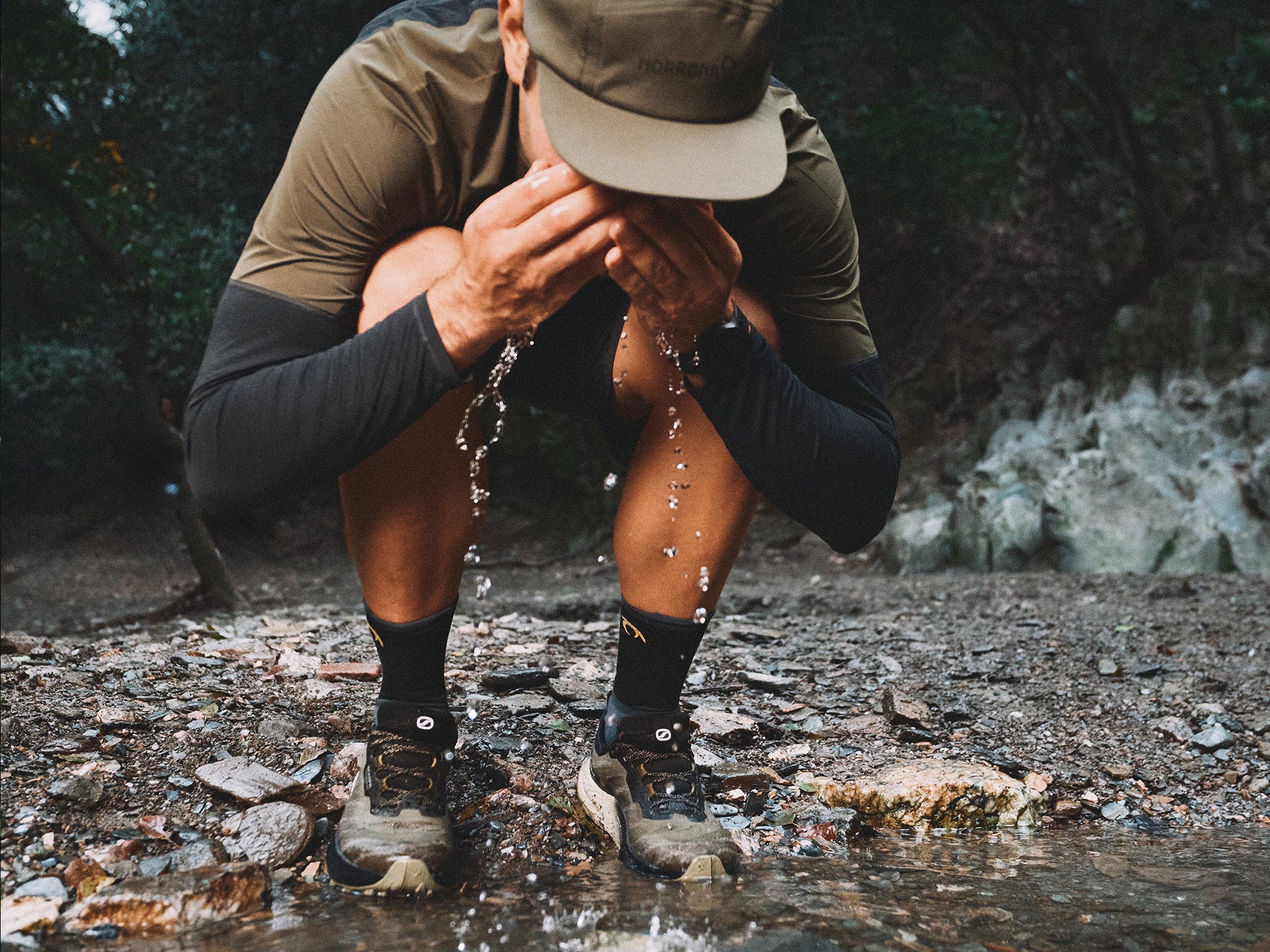 Trail runner crouching in a rocky stream, wearing SCARPA's Golden Gate LT WP trail running shoes.