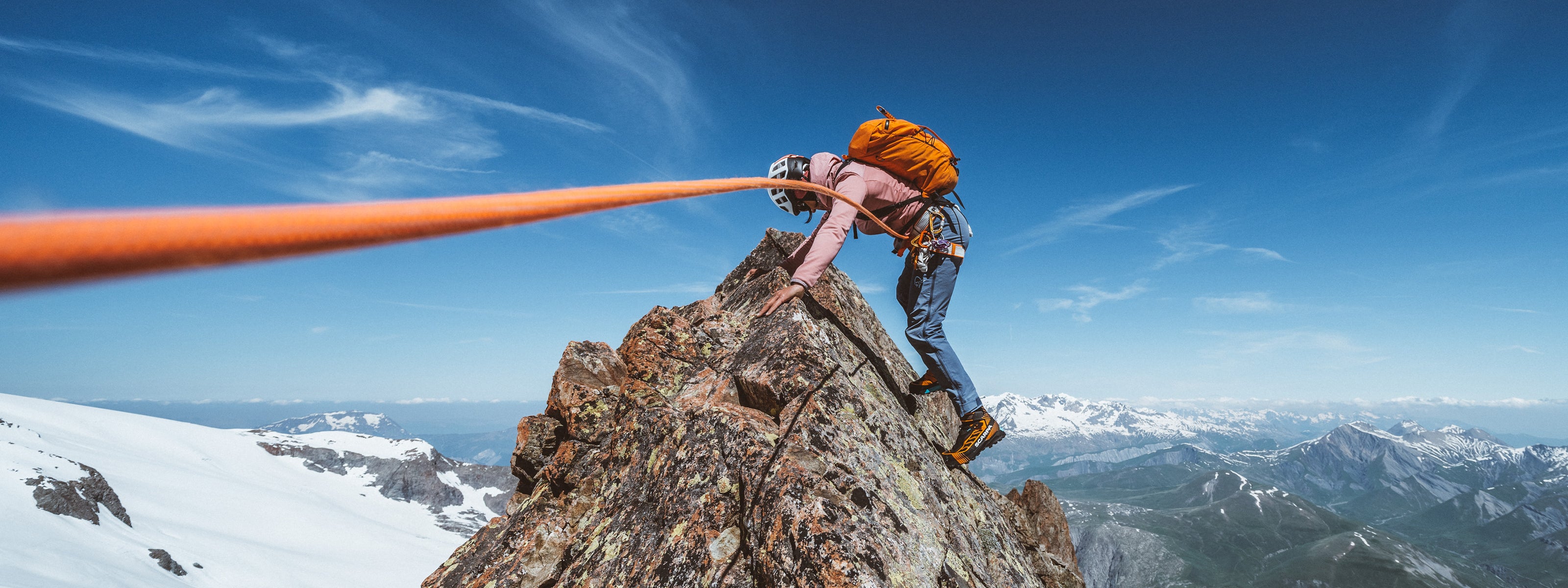 Mathieu Maynadier on a rocky mountain peak with a clear blue sky in the background with SCARPA Ribelle Tech 3 moutaineering boots