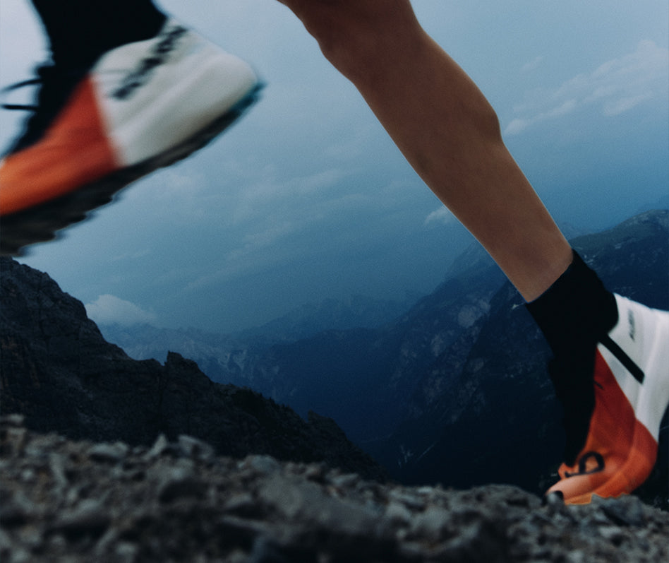 A close-up action shot of a trail runner's legs and feet wearing SCARPA's Alien Sky trail running shoes on a rocky mountain ridge.