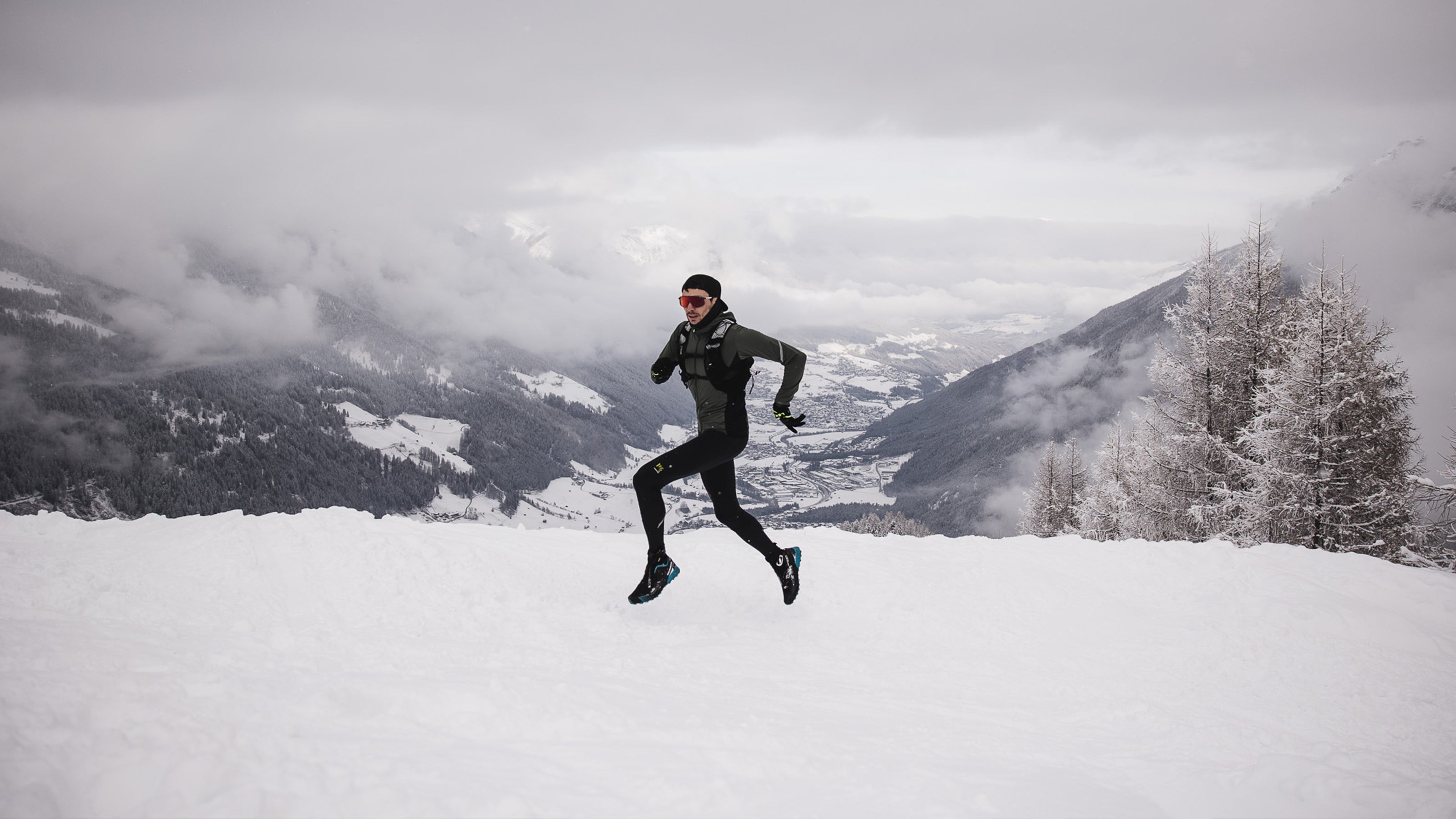 Trail-runner on a snow-covered landscape with mountains in the background wearing SCARPA's KALIBRA G trail running shoes