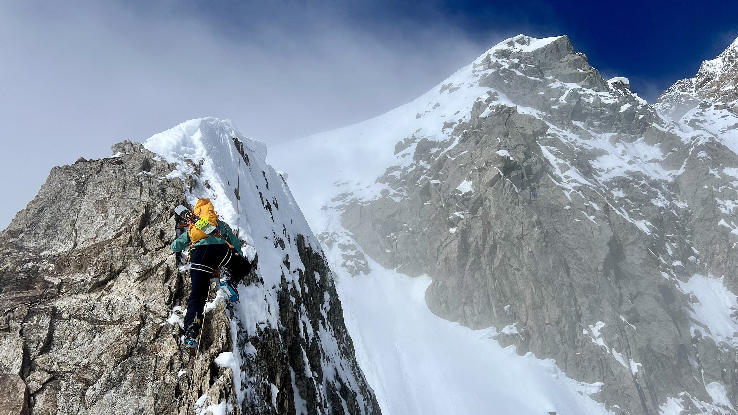 Damien Arnaud climbing Punta Innominata on Mont Blanc, ascending a steep snowy and rocky ridge under a clear sky.
