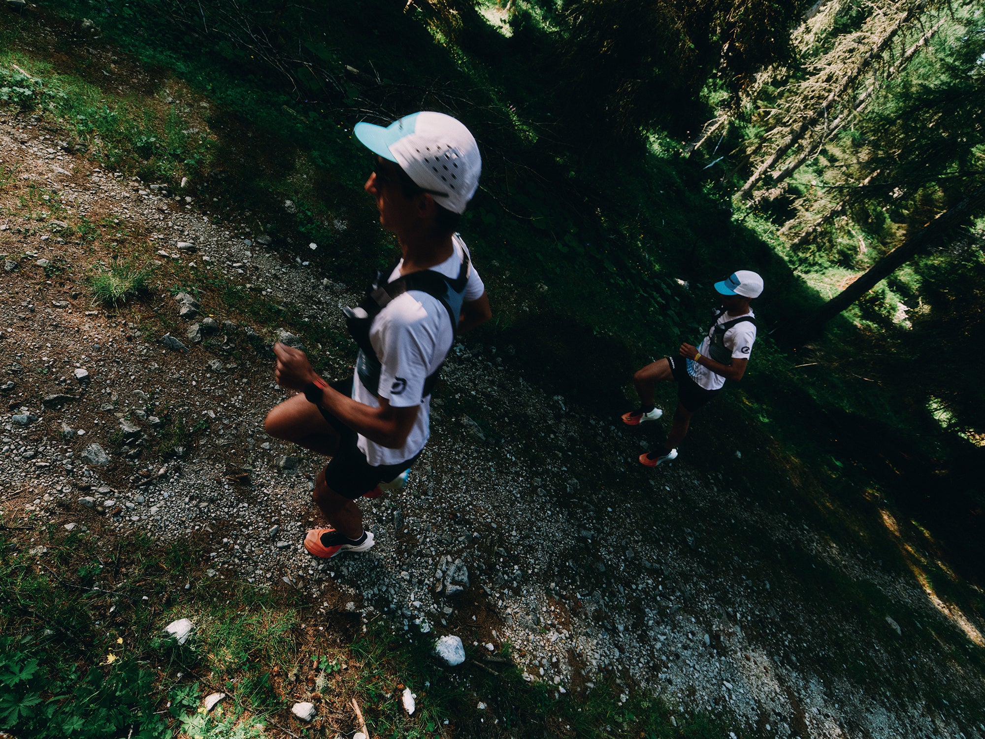 Two trail runners on a rocky forest path wearing SCARPA's Alien Ultra trail running shoes.