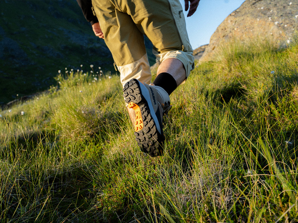Person hiking on a grassy hillside wearing SCARPA Mustang TRK GTX trekking boots.