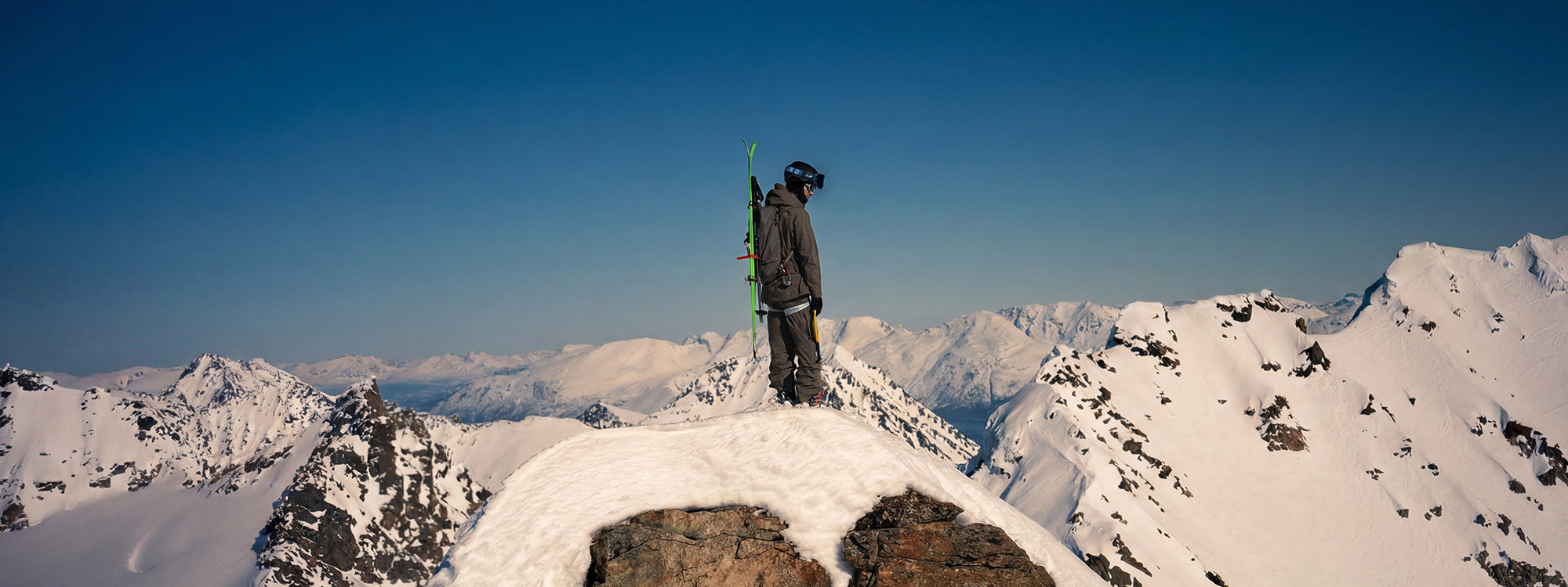 A skier stands on a snowy mountain peak with snow-covered peaks wearing SCARPA's Maestrale RS ski mountaineering boots.