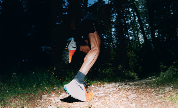 A low-angle action shot of a trail runner on a forest trail, wearing SCARPA Alien Ultra trail running shoes.