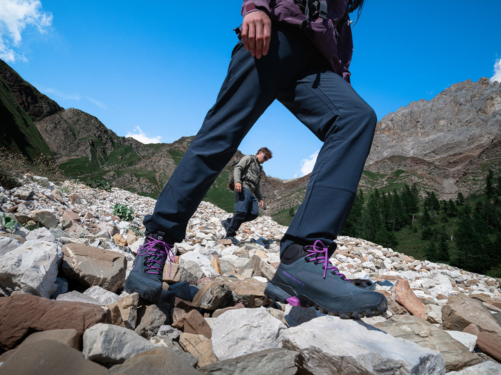 A close-up outdoor shot of a person hiking up a rocky mountain slope, wearing SCARPA Ribelle Cross 2 Mid GTX light hiking boots.