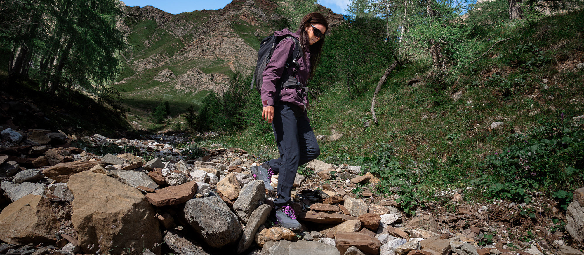A woman hiking through a rocky mountain stream, wearing  SCARPA Ribelle Cross 2 Mid GTX light hiking boots.