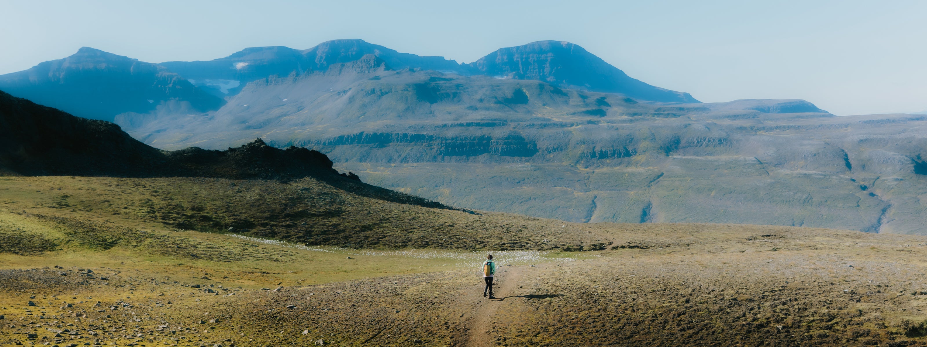 Hiker standing on a dirt path in a vast, open landscape with mountains in the background wearing SCARPA's Rapid XT approach shoes