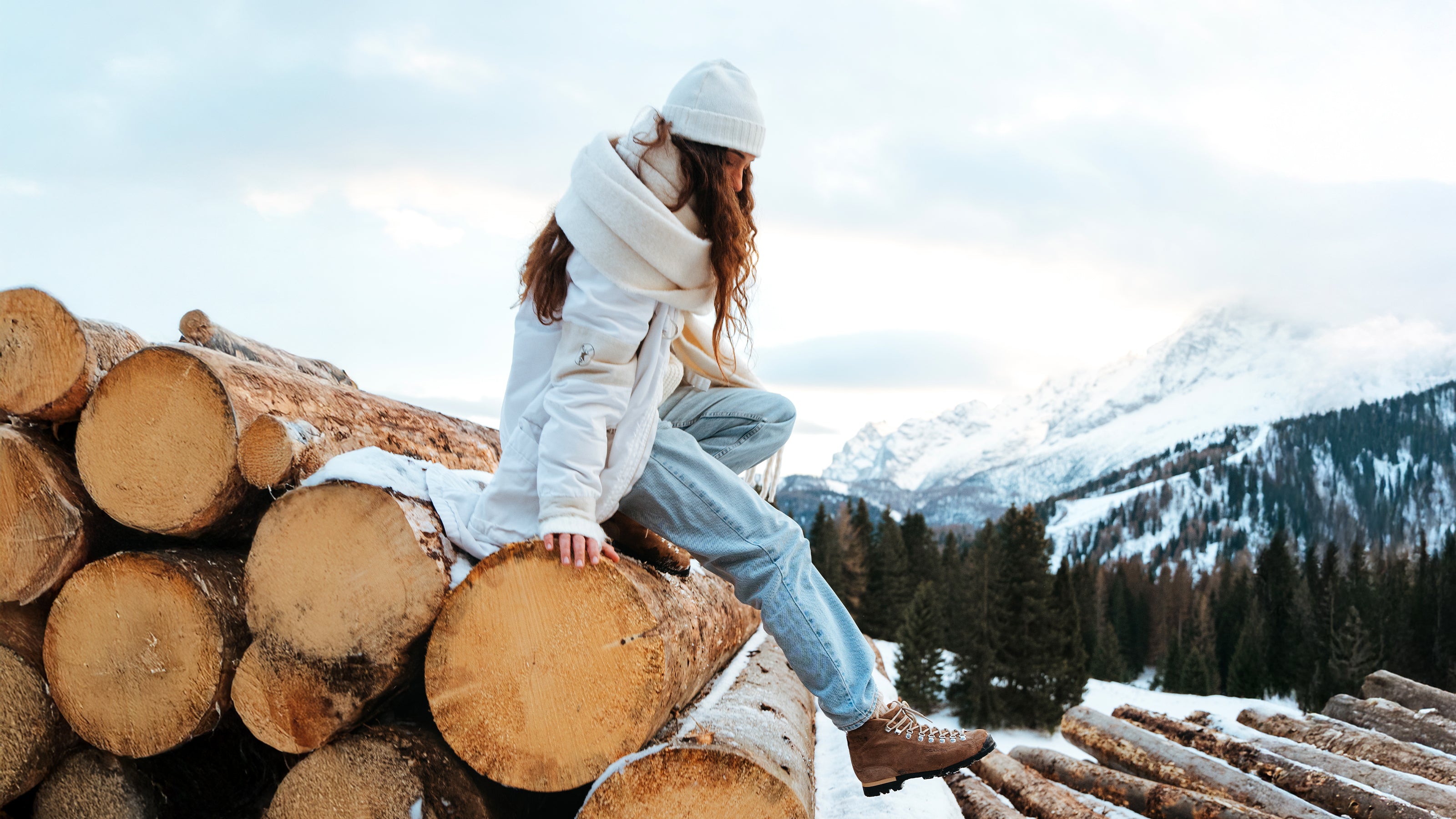 Person sitting with snowy mountains in the background wearing SCARPA PRIMITIVE winter collection shoes